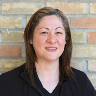 Professional headshot of woman smiling against brick wall background for dental practice.