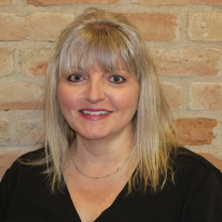 Professional headshot of woman with blonde hair against brick wall background, Hamilton Dental staff photo.