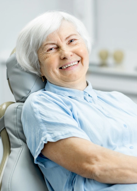Smiling senior woman relaxing in dental chair wearing light blue bib at Hamilton Dental office.