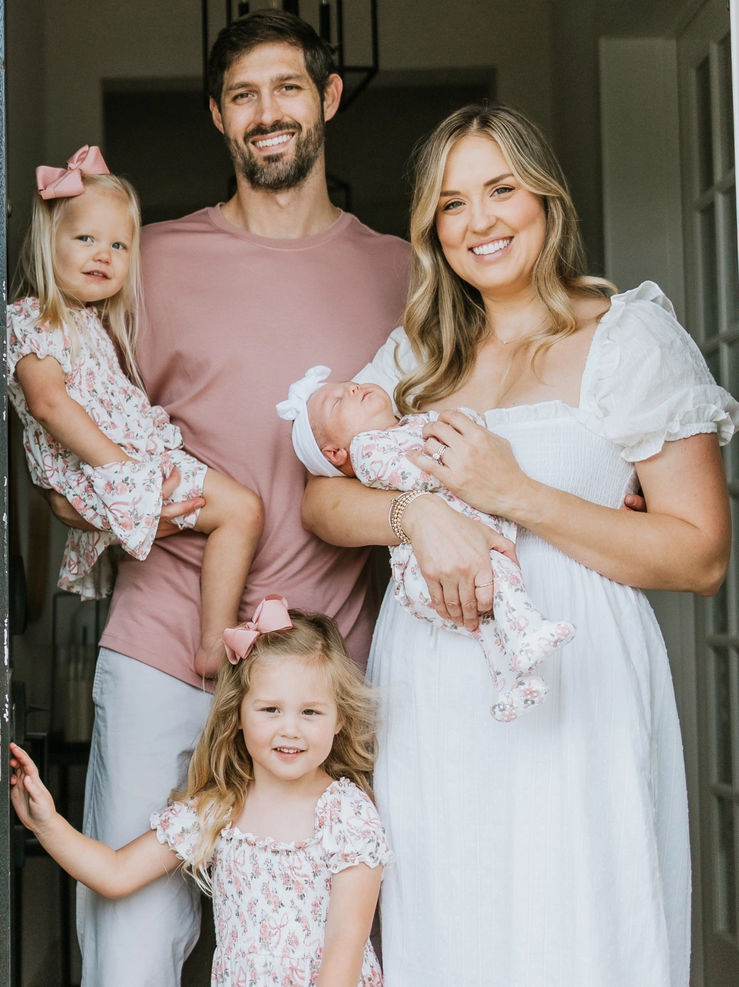 Family of four smiling together in home doorway, dressed in coordinated pastel outfits.